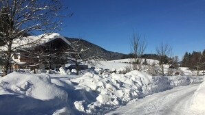 A snow-covered road with a building and trees in the background. - Vacation apartment Kienberg for 2 persons, 45 sqm, eat-in kitchen, with balcony (Inzell)