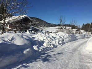 A snow-covered road with a building and trees in the background.