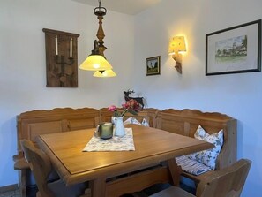 Un comedor con una mesa de madera y bancos, una lámpara colgante, luces de pared y un cuadro enmarcado.