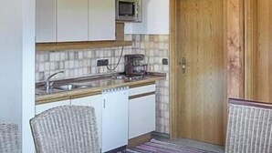 A compact kitchen with white cabinets, a microwave, a coffee maker, and a dishwasher. There is a wooden door and wicker chairs. - Vacation apartment 9 for 4 people in the attic, 2 bedrooms, balcony, 82 m² (Inzell)