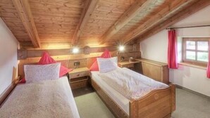 A room with two wooden beds, a wooden ceiling, and a window with a red curtain. - Vacation apartment 9 for 4 people in the attic, 2 bedrooms, balcony, 82 m² (Inzell)