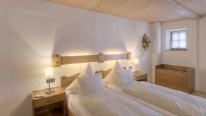 A bedroom with a wooden ceiling, a bed with white bedding, two bedside tables with lamps, and a window with a view of the outside. - Vacation apartment 4 for 2 persons, 1 bedroom, upper floor, balcony, 53 m² (Inzell)