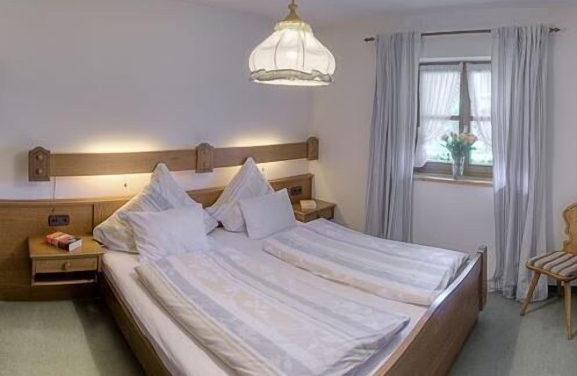 A double bed with a wooden headboard, a bedside table with a lamp, and a window with curtains.