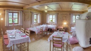 Un comedor de madera con varias mesas dispuestas para comer, con manteles a cuadros y cojines rosados.