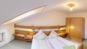 Un dormitorio con techo inclinado, una cama con ropa de cama a rayas, un armario de madera y una mesita de noche con lámpara.