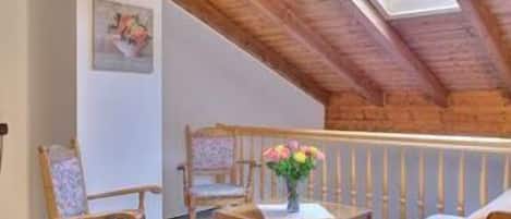 Cozy attic retreat with a sloped ceiling, wooden beams, and a skylight, featuring a sofa, chairs, and a small table.
