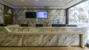 A reception desk with a marble wall, a digital screen, and a window with a view of palm trees. - City Comfort Inn (Zhuhai Qinglv Middle Road) (Zhuhai)