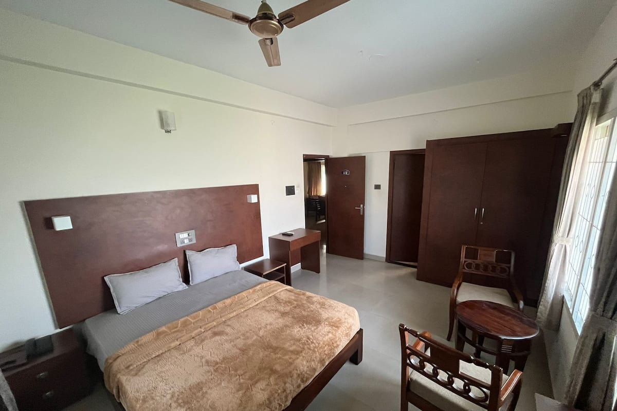 Une chambre d’hôtel équipée d’un lit, d’un bureau, d’une chaise, d’une armoire et d’un ventilateur de plafond.