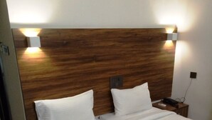 Una habitación de hotel con dos camas, cabecero de madera, ropa de cama blanca y lámparas de noche.