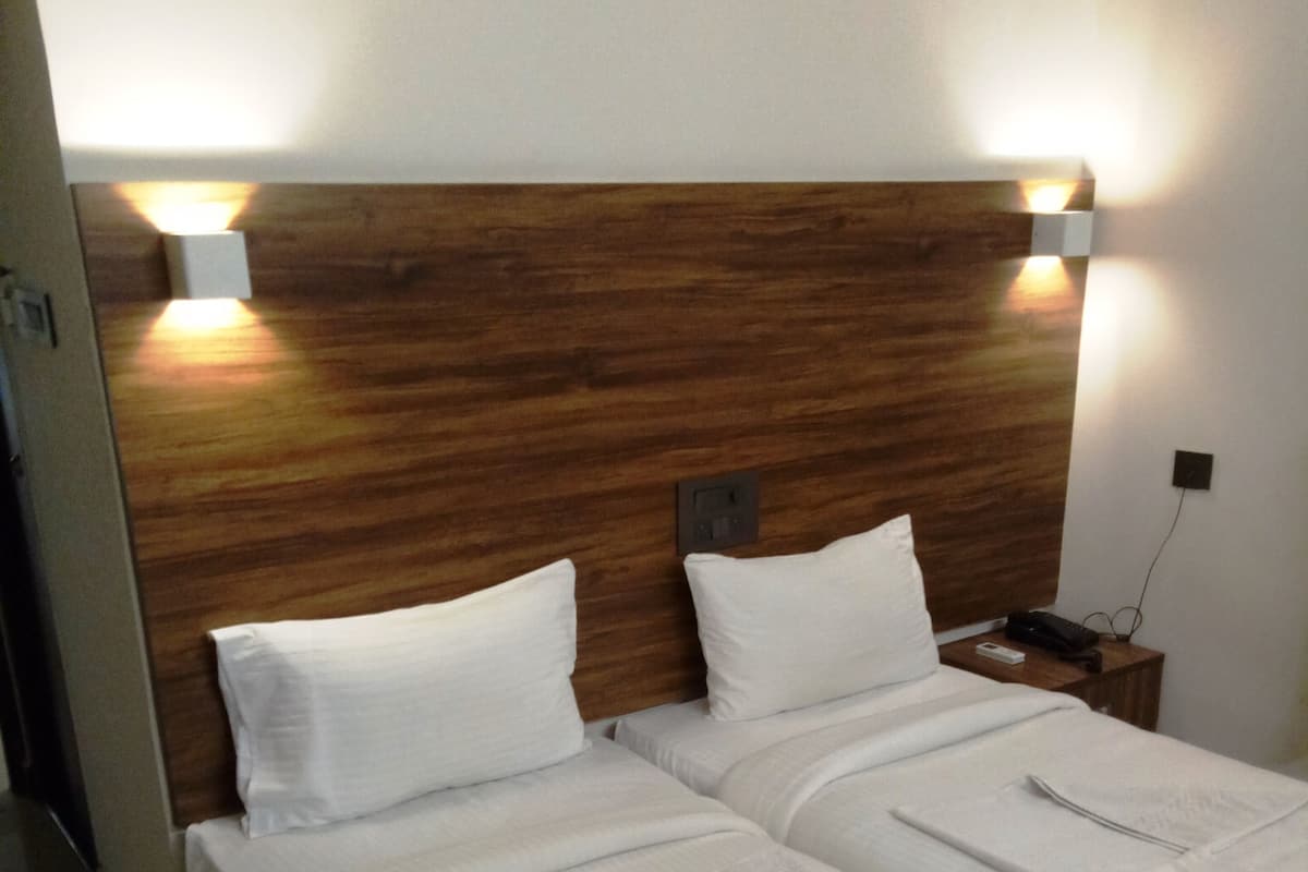 Une chambre d’hôtel avec deux lits, une tête de lit en bois, du linge de lit blanc et des lampes de chevet.
