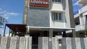 Un edificio moderno con un letrero que dice “Athithi Inn”. Presenta una combinación de materiales de piedra y hormigón, varios balcones y una zona de entrada cubierta.