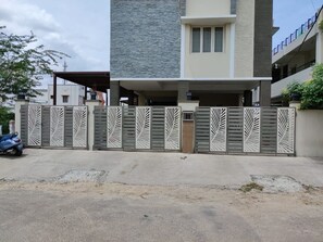 Un edificio residencial moderno con entrada protegida por un portón, zona de estacionamiento techada y una patineta azul a la vista.