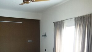Una sala de estar con un sofá, dos sillones, una mesa de madera, un ventilador de techo y una ventana con cortinas.