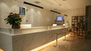 A modern reception area with a marble counter, a television, and a seating area with a bookshelf. - Shankee Tea Style Hotel (Danyang Economic Development Zone) (Danyang)