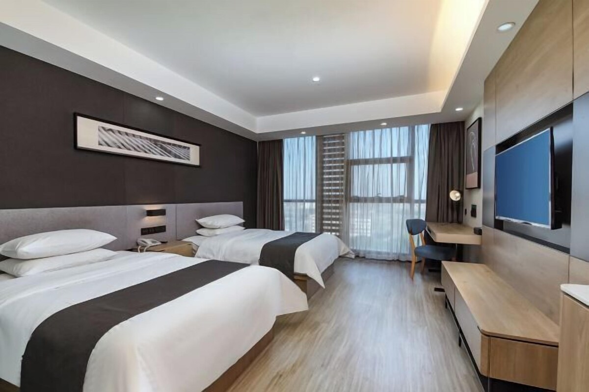 Habitación de hotel con dos camas, un escritorio, un televisor y un ventanal con cortinas.