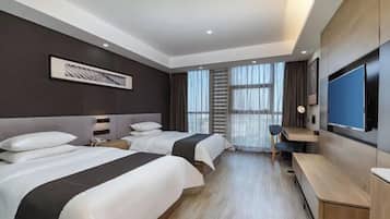 Quarto de hotel com duas camas, uma escrivaninha, televisão e uma janela grande com cortinas.