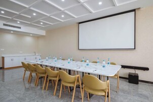 Una sala de conferencias con una larga mesa, sillas, una pantalla de proyector y una pizarra.