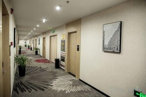 A hotel corridor with doors, a patterned carpet, potted plants, and a framed picture on the wall. - Shankee Tea Style Hotel (Danyang Economic Development Zone) (Danyang)