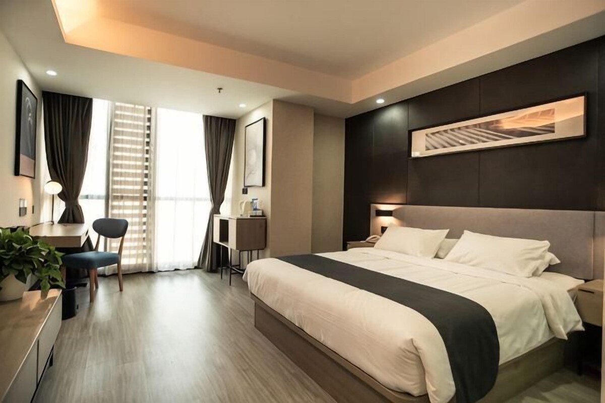 A modern hotel room with a large bed, a desk, a chair, and a view of the outside.