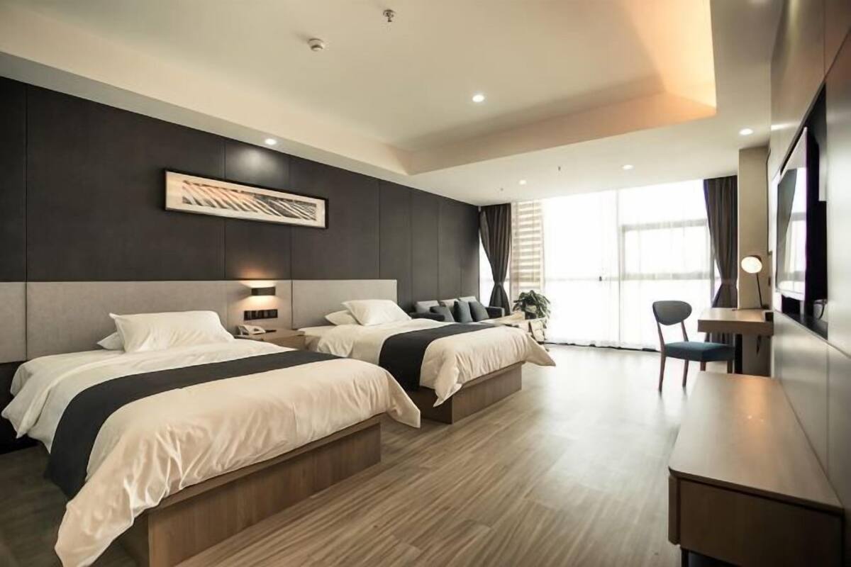 Una habitación de hotel moderna con dos camas, un escritorio y un ventanal grande.
