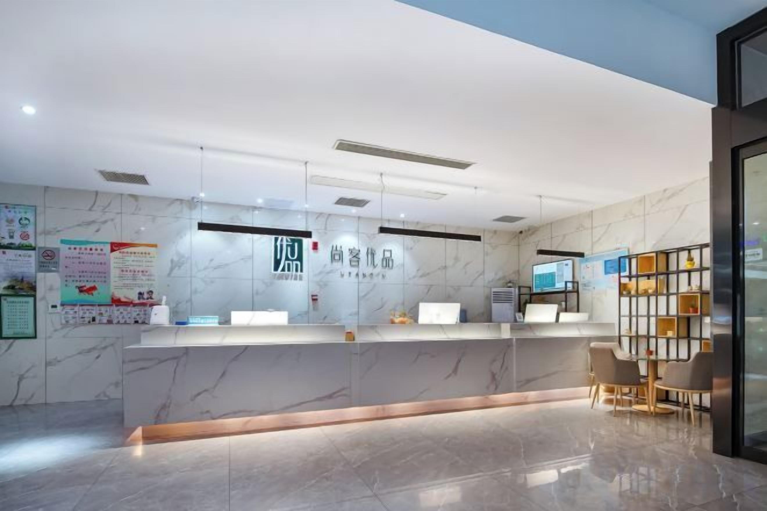 A hotel reception area with a marble reception desk, a digital screen, and a seating area with a small table and chairs.