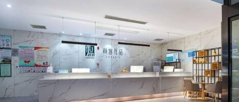 A hotel reception area with a marble reception desk, a digital screen, and a seating area with a small table and chairs.