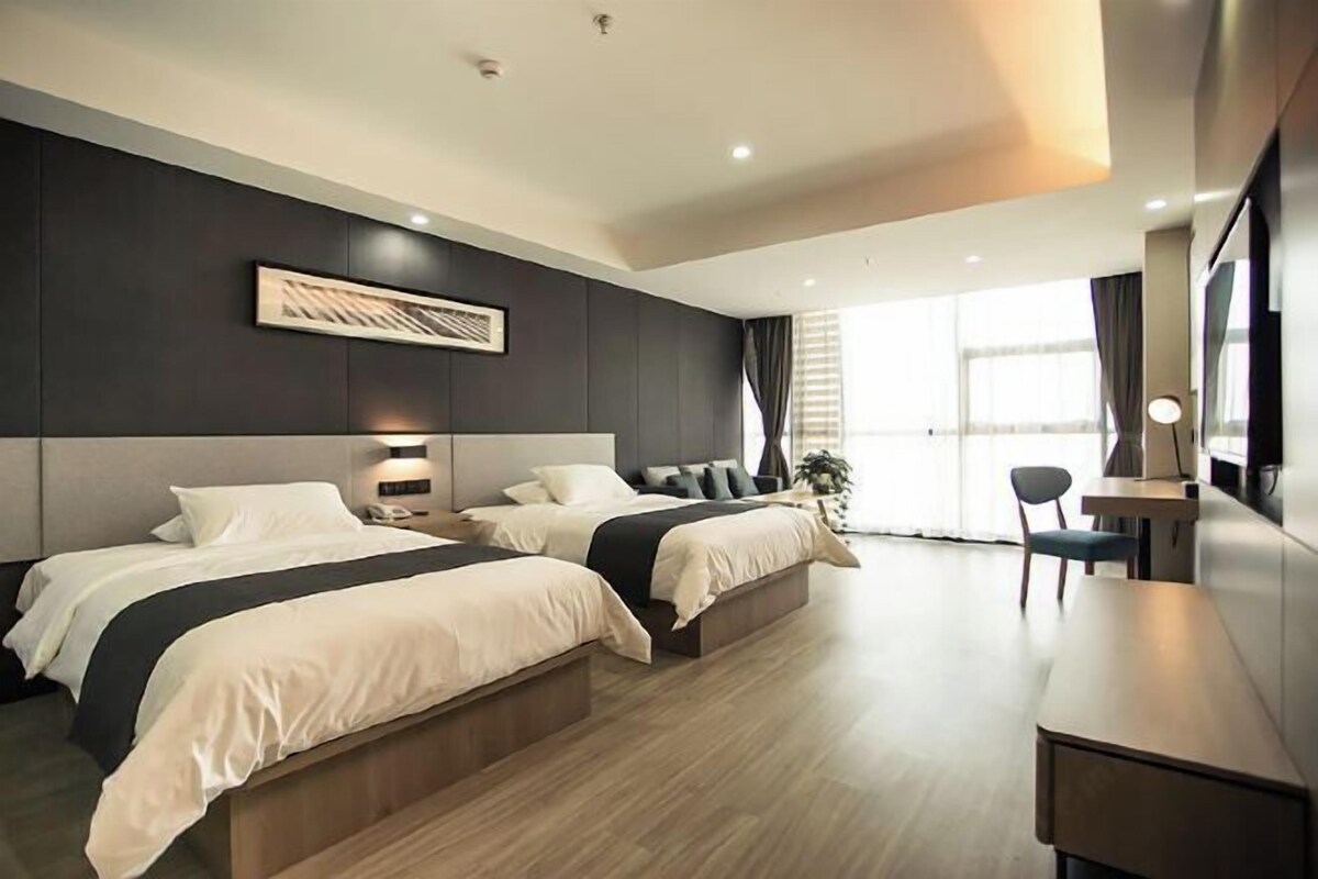 Una habitación de hotel moderna con dos camas, un escritorio y un amplio ventanal.