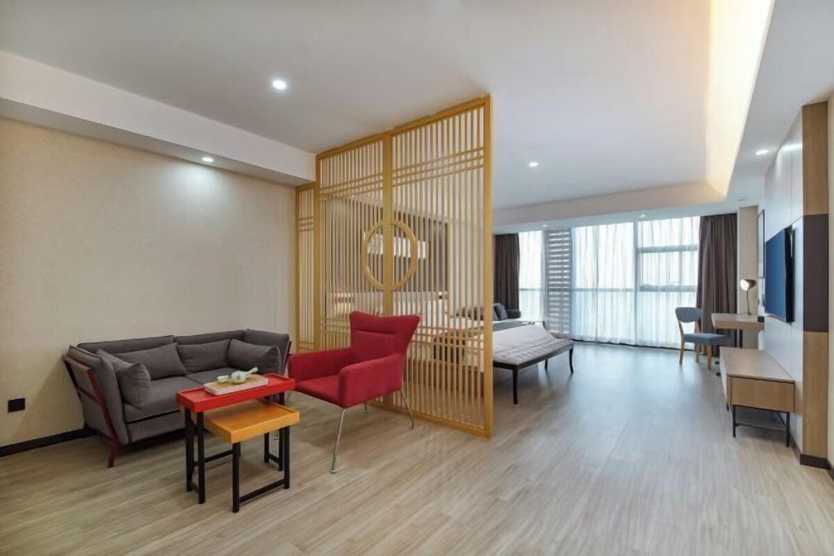 Una sala de estar moderna con un sofá, un sillón rojo, un separador de madera y un televisor.