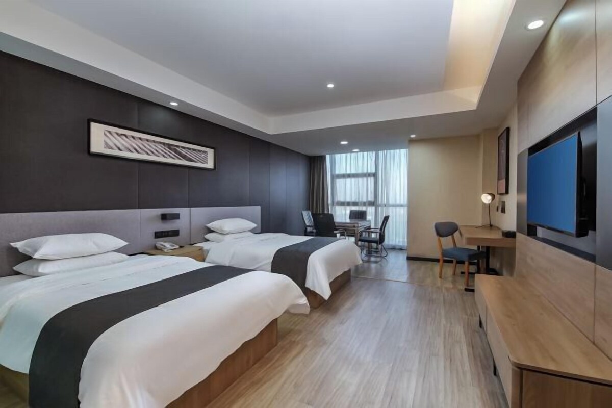 Habitación de hotel con dos camas, un escritorio, una silla, un televisor y una ventana con cortinas.