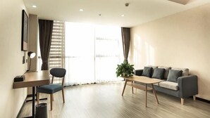 A modern living room with a sofa, a coffee table, a desk with a chair, and a large window with curtains. - Shankee Tea Style Hotel (Danyang Economic Development Zone) (Danyang)