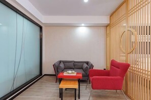 A modern living room with a grey sofa, a red armchair, a small wooden table with a book and a teapot, and a wooden partition with a circular cutout. - Shankee Tea Style Hotel (Danyang Economic Development Zone) (Danyang)