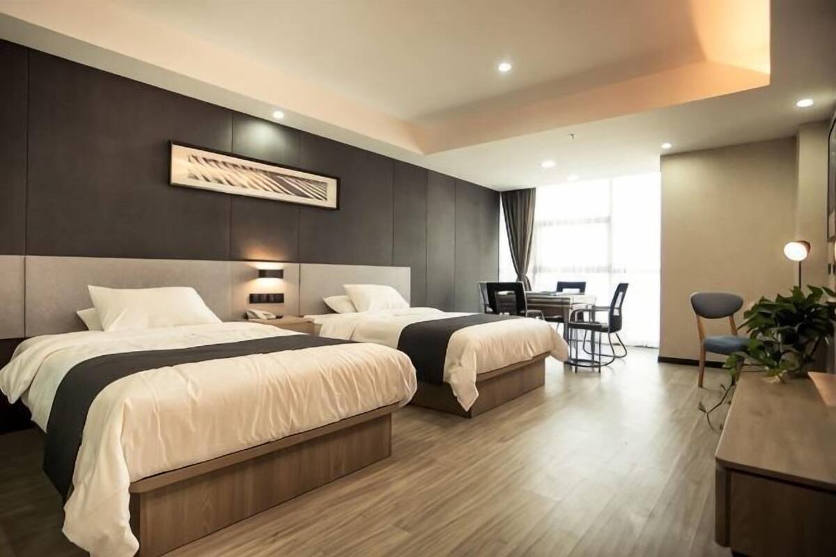 Una habitación de hotel moderna con dos camas, una zona de comedor y un ventanal grande.