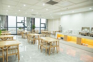 Uma sala de jantar espaçosa com várias mesas e cadeiras de madeira, um balcão com detalhes em amarelo e grandes janelas que oferecem uma vista.