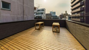 A rooftop terrace with a wooden floor, two wooden tables, and a view of city buildings. - Yadoya Fukurou (Tokyo)