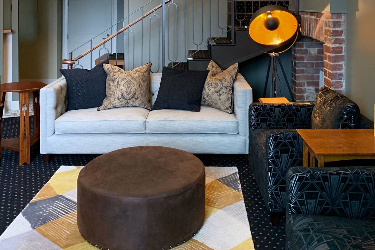 A modern living room with a sofa, ottoman, and patterned rug. A staircase with metal railings leads to an upper level.
