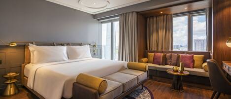 A modern hotel room with a large bed, a sofa, a desk, and a view of the city.