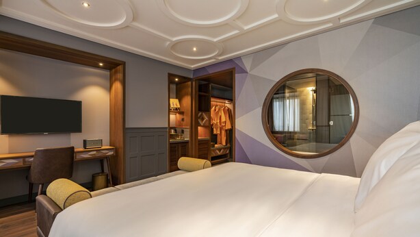Ein Hotelzimmer mit einem großen Bett, einem Schreibtisch mit Stuhl, einem Fernseher und einem Kleiderschrank.