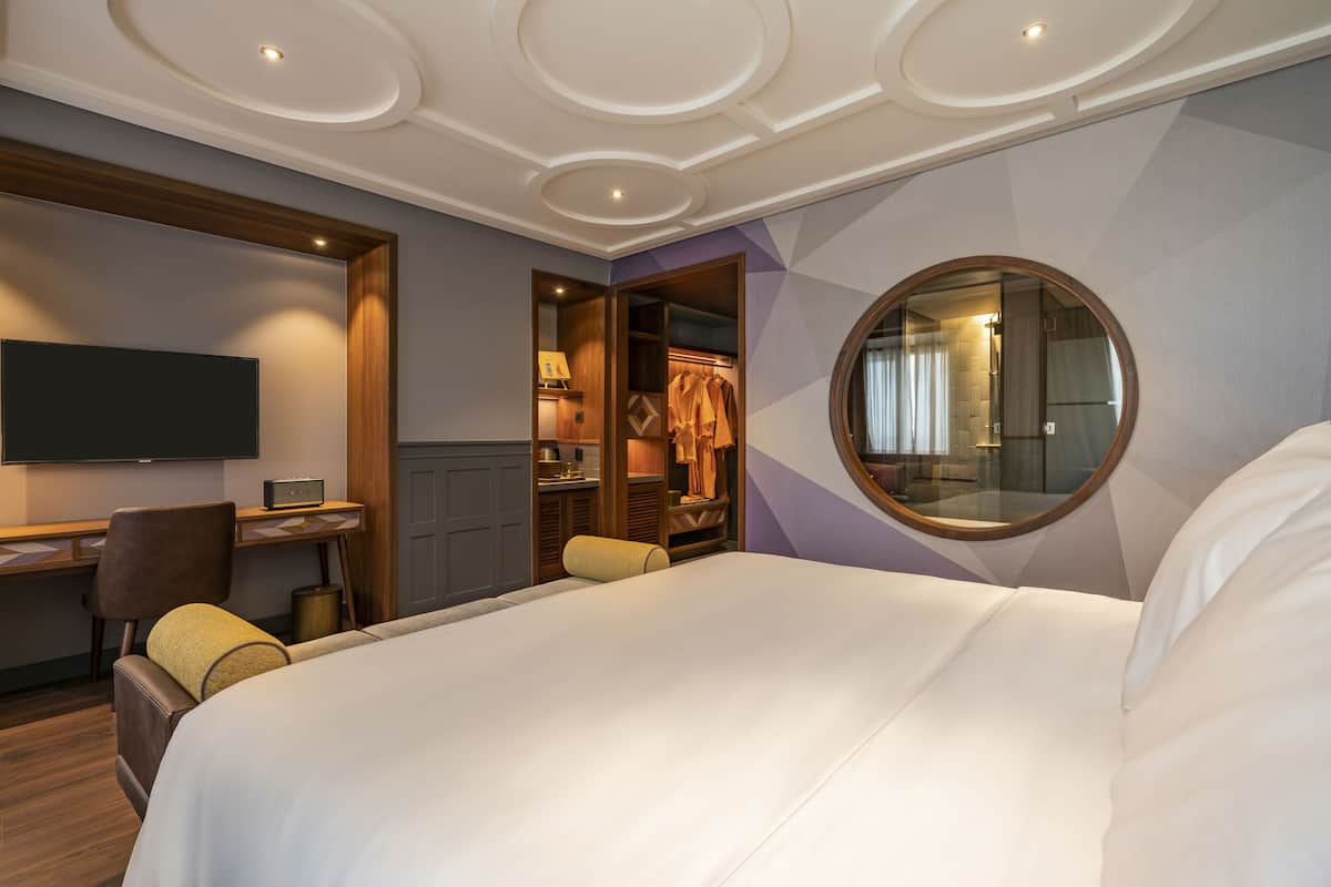 A hotel room with a large bed, a desk with a chair, a TV, and a wardrobe.