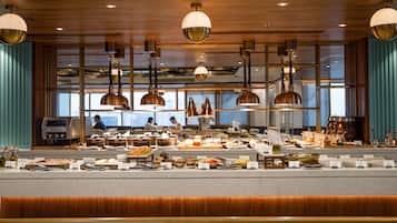 A buffet setup with various food items and a coffee station, wooden paneling, and pendant lighting.