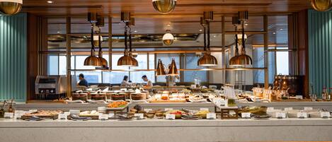 A buffet setup with various food items and a coffee station, wooden paneling, and pendant lighting.