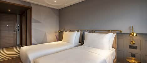 Een moderne hotelkamer met twee bedden, een houten deur, een kamerkleed met patroon en een gouden accent op het nachtkastje.