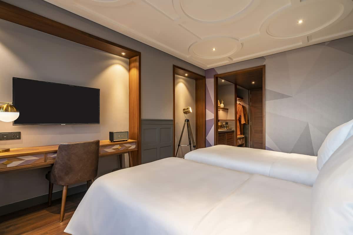 A hotel room with a large bed, a desk with a chair, a television, and a wardrobe.
