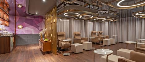 A modern spa with a wooden floor, a reception area with a counter and shelves, and multiple seating areas with chairs and tables.