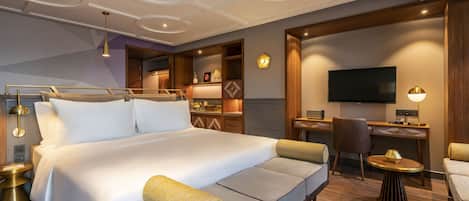 A modern hotel room with a large bed, a desk, a TV, and a seating area.