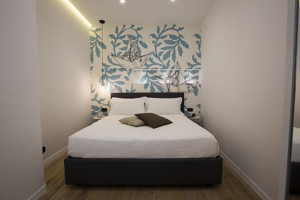 Een moderne slaapkamer met een bed, nachtkastjes en een muur met bladmotieven.