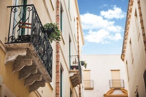 Una calle estrecha con edificios que tienen balcones con barandillas de hierro forjado y plantas en macetas.