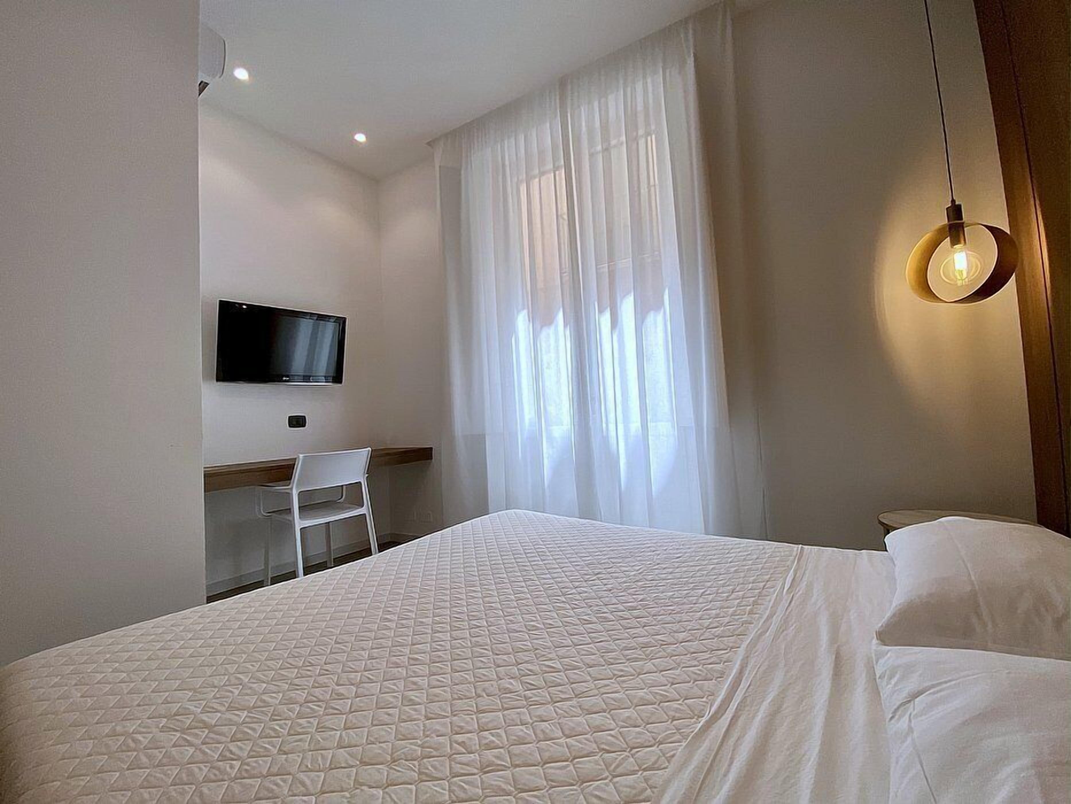 A hotel room with a bed, a desk, a chair, a television, and a window with curtains.