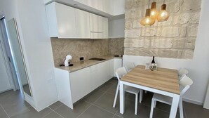 A modern kitchen with white cabinetry, a wooden dining table, and a stone accent wall. - Appartamento Anice B: A welcoming apartment situated in a central location, at a short distance from the main tourist attractions of the city, with Free WI-FI. (Trapani)