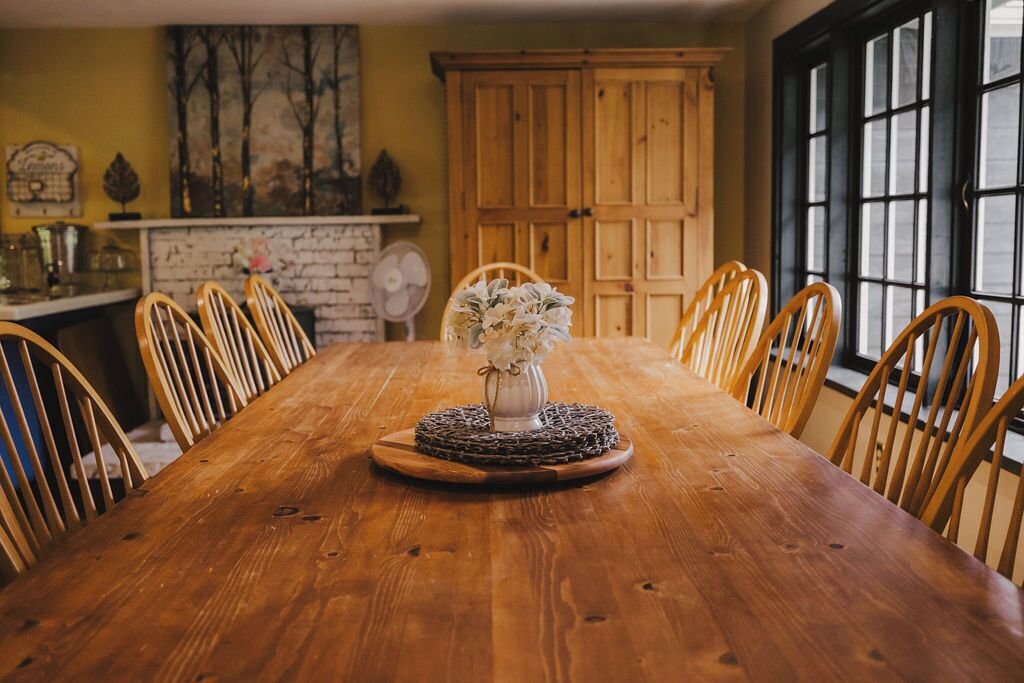 A wooden dining table with a vase of flowers in the center, surrounded by wooden chairs.