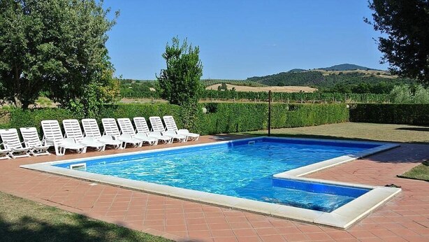 A rectangular swimming pool with a tiled deck, surrounded by white lounge chairs, set against a backdrop of hills and vineyards.